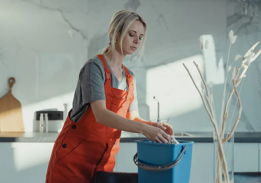 Intervenante en tenue orange effectuant le ménage dans une cuisine lumineuse — AXEO Services à Houilles